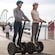 2 people in helmets each riding a motorized 2 wheel transporter
